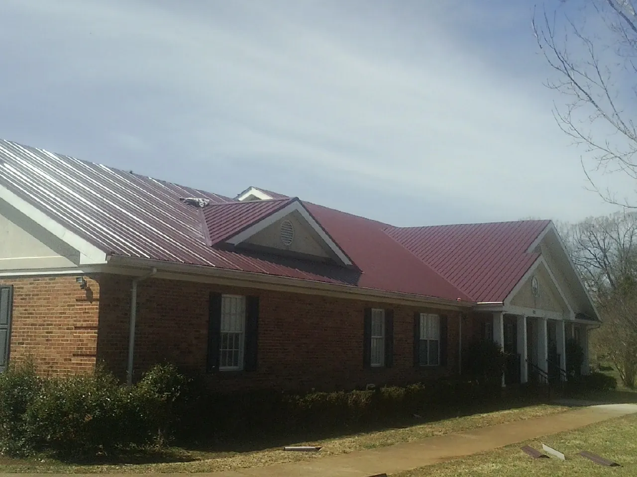 Red metal roof with gabled entries on a long brick building, from a Hail Damage Roof Repair job in Dover