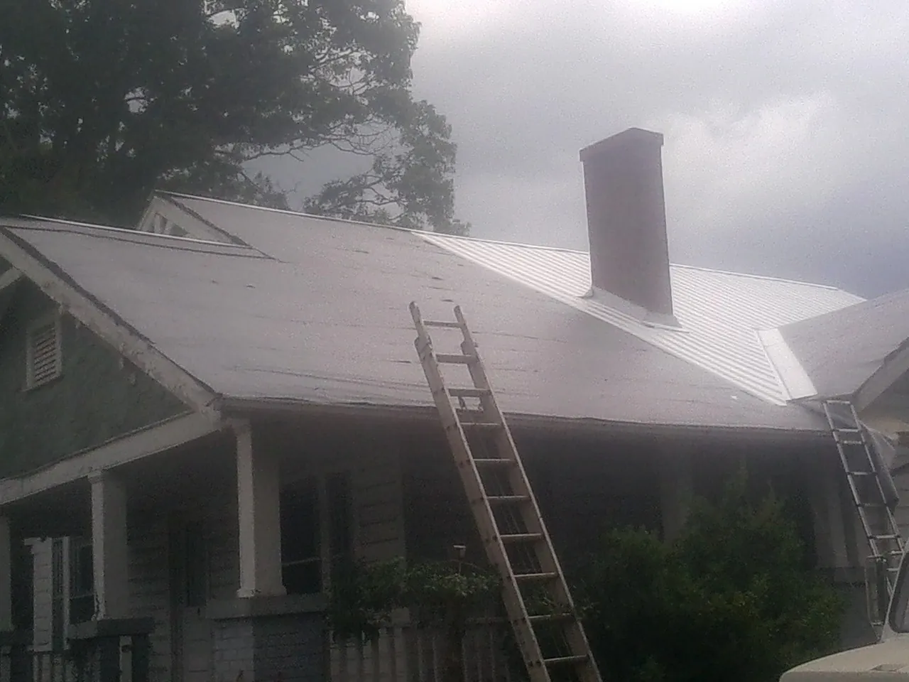 Ladders against a metal roof on an older home with a brick chimney in Dover